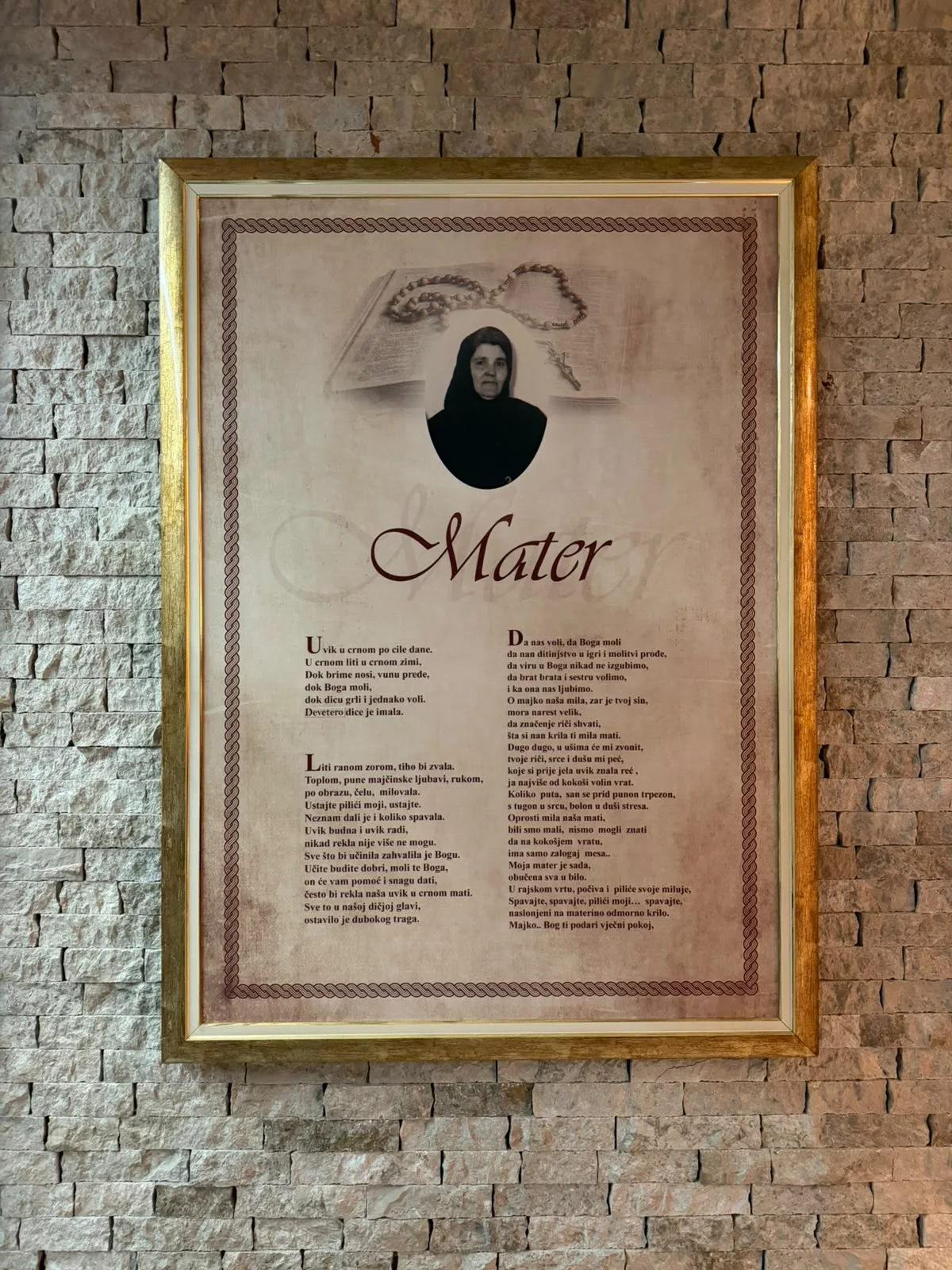 Uokvirena posveta materi na kamenom zidu restorana — fotografija matere u crnom i pjesma njoj u čast